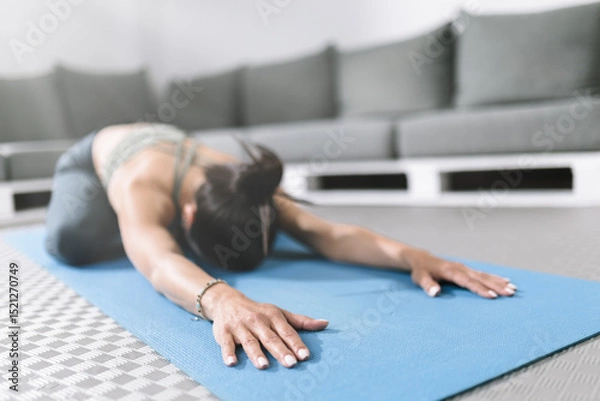 Obraz Practicing yoga with a child pose on a blue mat in a cozy indoor space with comfortable seating