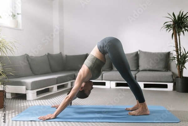 Obraz Woman practicing downward-facing dog pose in modern living room filled with plants and comfortable seating