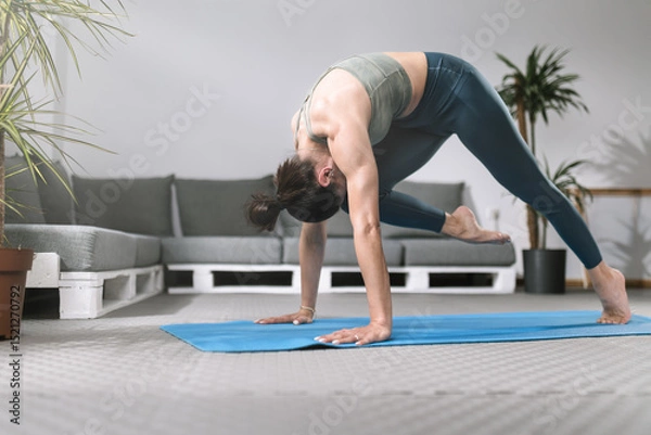 Obraz Woman practicing advanced yoga pose on mat in modern indoor space with plants and comfortable seating