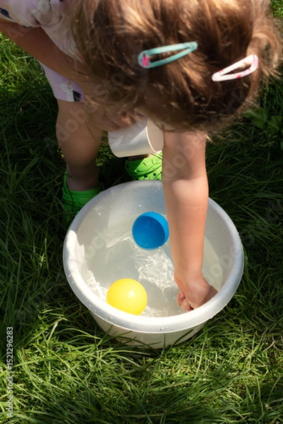 Fototapeta A child's hand reaches for the colorful balls floating in the water.