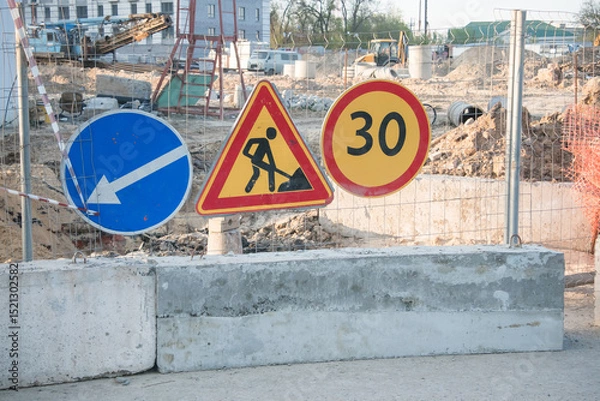 Fototapeta Construction site with traffic signs indicating direction and speed limit near urban area during daylight hours