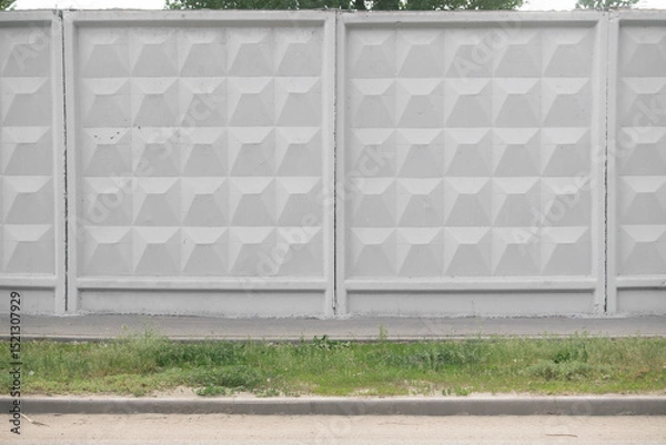 Fototapeta Textured concrete wall with geometric patterns, featuring a smooth gray surface and grassy area below, creating a modern urban aesthetic with copy space for design