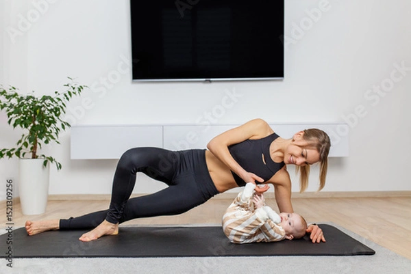 Fototapeta Morning routine. Active mom doing plank and playing with baby