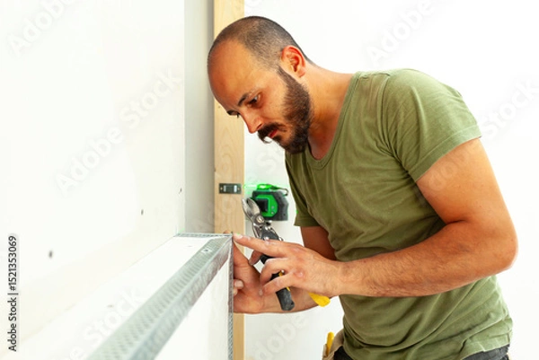 Fototapeta Construction Worker Installing Metal Corner Bead on Drywall Using Snips