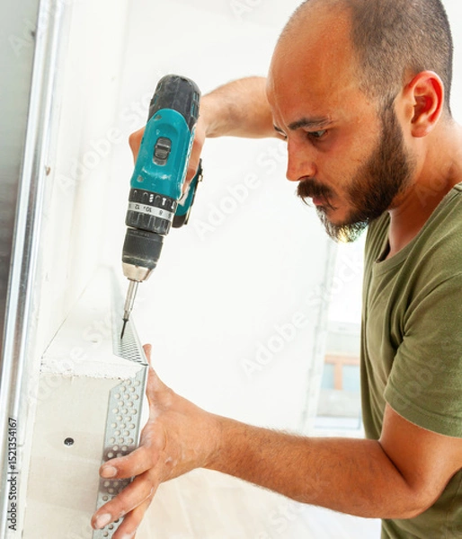 Fototapeta Construction worker installing drywall corner bead using cordless screwdriver