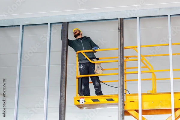 Fototapeta Construction worker installing drywall on a mobile elevating work platform