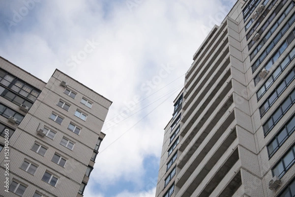 Fototapeta Modern residential buildings reaching towards the sky, showcasing architectural design and urban living with a backdrop of cloudy blue sky