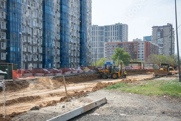 Fototapeta construction of a road near a large multi-storey residential building using two tractors with large iron buckets