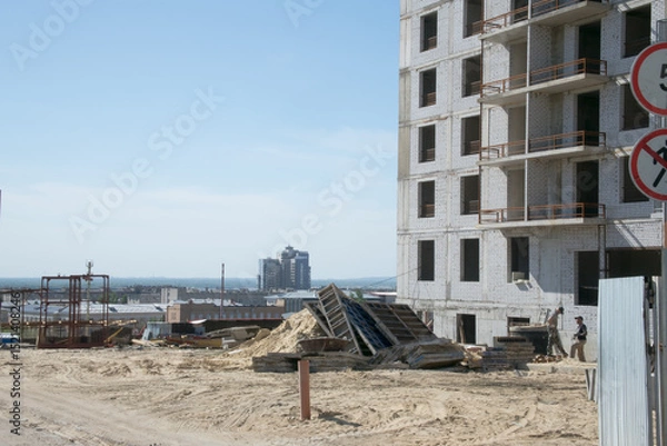 Fototapeta construction site near a large multi-storey grey brick apartment building with unglazed windows against the background of the city
