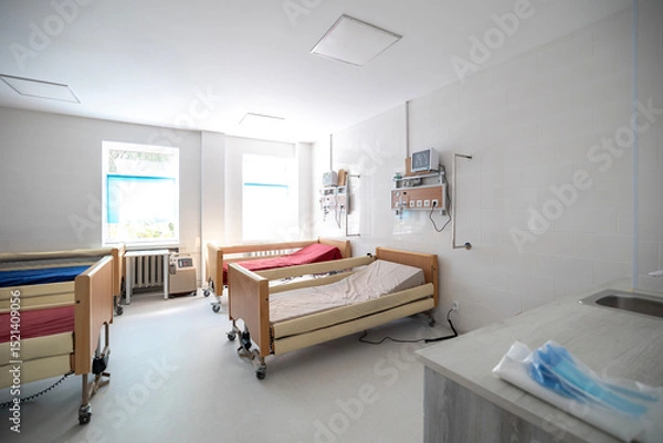 Fototapeta An oxygen hub with a flow meter and humidifier bottle is mounted on a wooden-paneled wall above a hospital bed in an intensive care unit