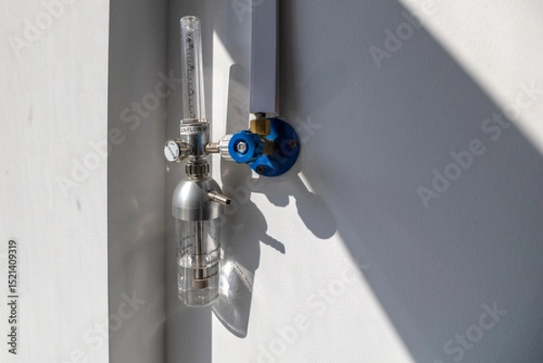 Fototapeta An oxygen flow meter with a humidifier bottle is mounted on a white wall, part of an oxygen hub, ready for use in a hospital intensive care unit.