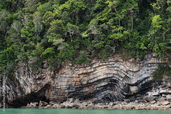 Obraz Series of layered stone slabs (Sedimentary Process) covered with lush green forest and blue sea. Geological wonders :The rock formation found in middle of Khanom Sea in Thailand.  Pancake Rock 
