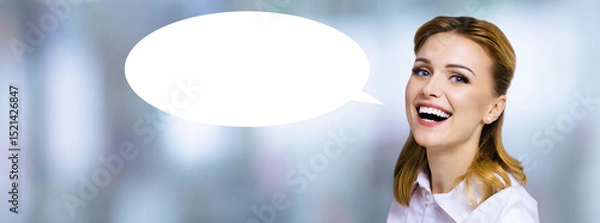 Fototapeta Wow! Portrait image of expressive emotional smiling young business woman with white empty mockup speech bubble. Happy cheerful cute blond hair girl against blurred modern office background