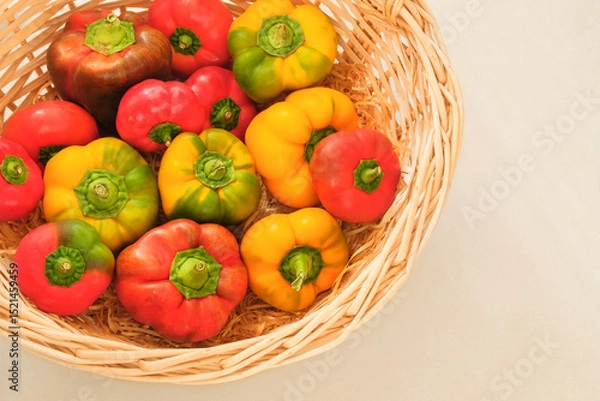 Obraz Orange and red ripe peppers. Sweet vegetables in a straw basket. Organic paprika. Top view. Place for text.