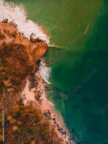 Fototapeta Top down view of rocky shore with ocean, waves and warm sun light