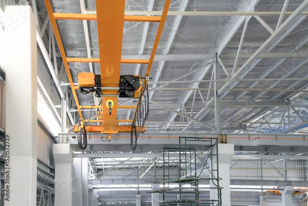 Fototapeta Overhead crane inside factory or warehouse building. Industrial machine or lifting equipment consist of hoist, hook and wire rope move on beam girder structure for manufacturing production plant.