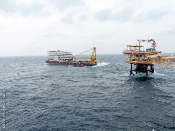 Obraz Offshore Platform Operation A large vessel approaches a towering offshore oil platform amidst a choppy sea under a cloudy sky. The scene depicts industrial activity at sea.
