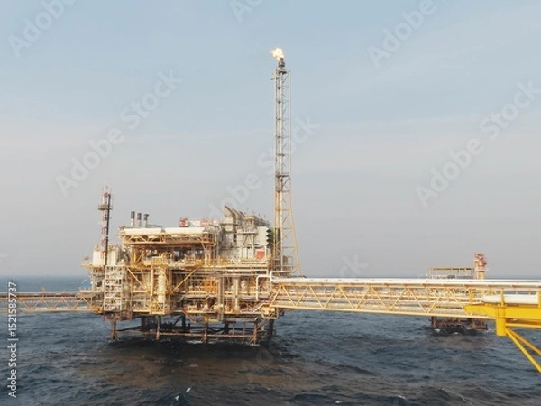 Obraz A majestic offshore oil platform stands tall against a serene, hazy sky, its flame a beacon in the vast ocean. The structure, complex and intricate, is a testament to human engineering prowess.