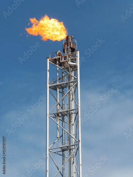 Obraz Industrial Flare Stack Against a Clear Blue Sky, Burning Brightly with a Large Flame, Illustrating Energy Production and Combustion Processes.