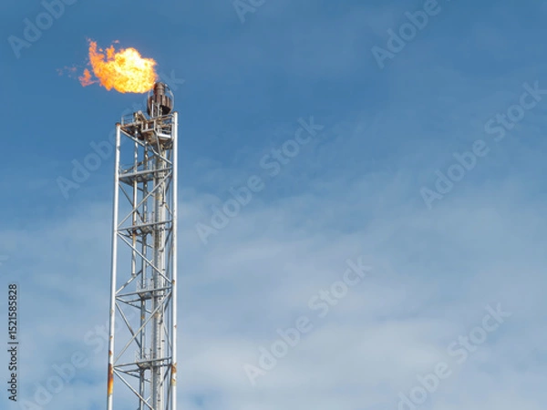 Obraz A metal tower with a bright flame burning at the top is set against a clear blue sky with light clouds. The tower appears tall and slender. The background is solid, not transparent. 