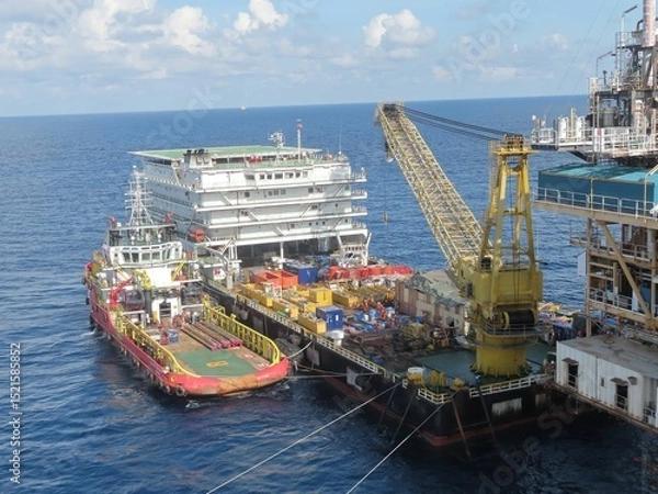 Obraz A massive offshore platform receives supplies via a specialized barge and crane, a testament to the intricate logistics of deep-sea operations under a partly cloudy sky.