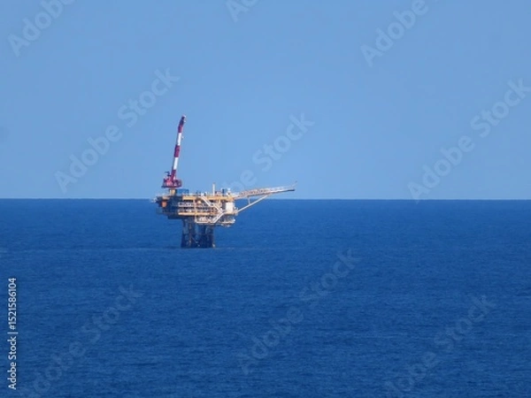 Obraz A lone offshore oil platform stands majestically in the vast, deep blue ocean under a clear, serene sky. The platform, a symbol of industry, contrasts sharply with the untouched beauty of nature.