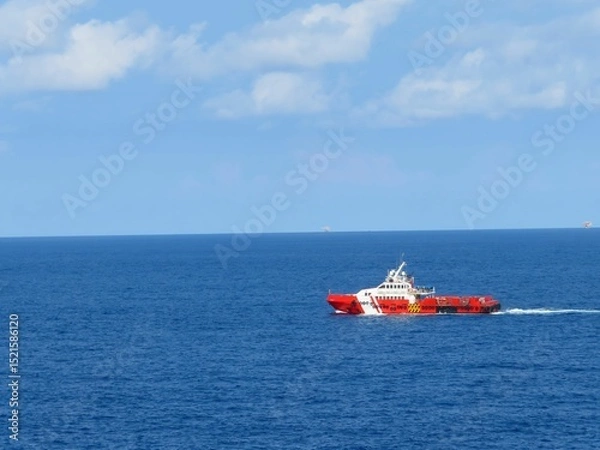 Obraz Red and white supply vessel navigates the deep blue ocean under a partly cloudy sky. A tranquil scene of maritime transport at sea.