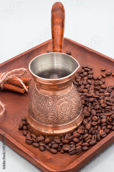 Fototapeta Copper coffee pot with coffee beans and cinnamon sticks. On a wooden plate board. White background