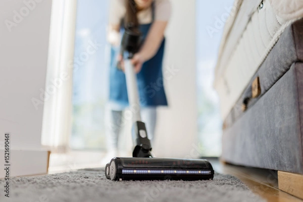 Obraz Woman vacuuming carpet in bright room during spring cleaning session at home