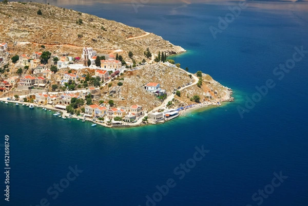 Fototapeta View of Ano Symi shore from a higher point, sun shines on traditional Mediterranean architecture building near sea