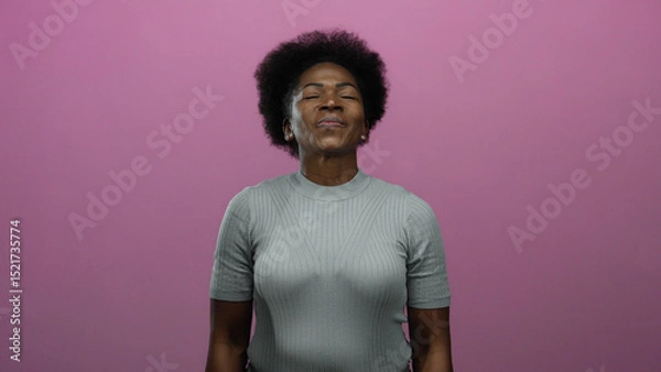 Fototapeta Woman enjoying peaceful moment standing on isolated pink background with eyes closed, conveying calm expression.