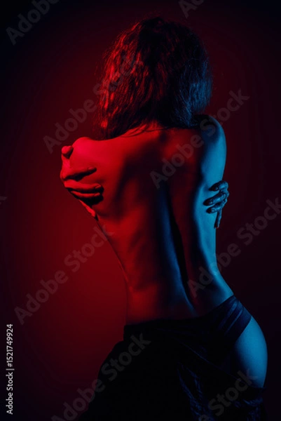 Fototapeta Woman studio posing with bare back, vibrant red and blue lights