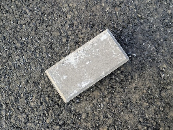 Fototapeta Close-up of a single weathered brick placed on asphalt background