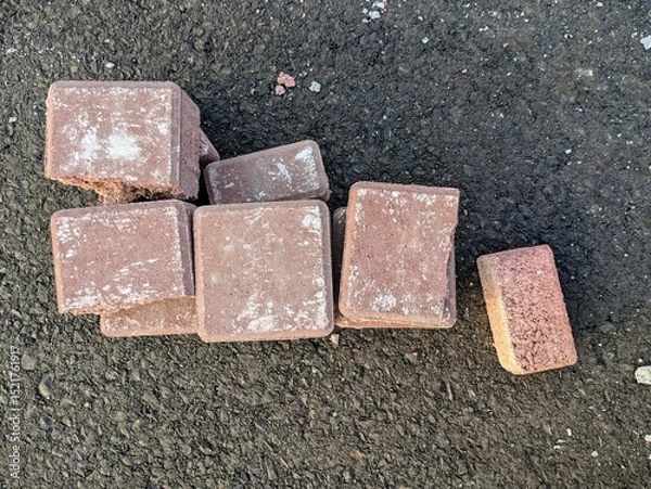 Fototapeta Stacked brown pavement bricks on black asphalt ground surface