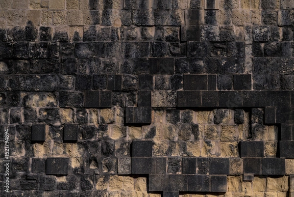Fototapeta Close-up of dark textured stone wall with black rectangular blocks. Ideal for architectural presentations, construction brochures, or design mockups needing rugged texture.
