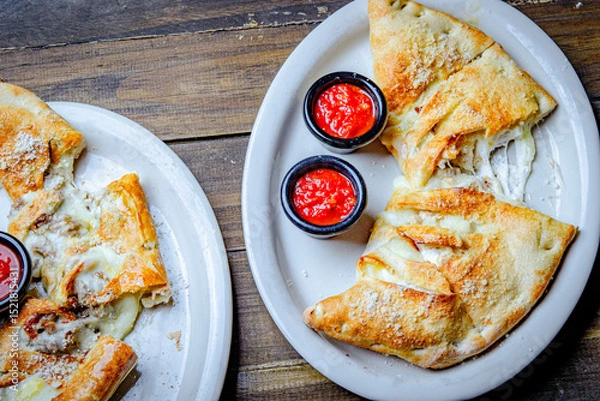Fototapeta Stromboli stuffed with cheese and pepperoni served with a side of ketchup cups.