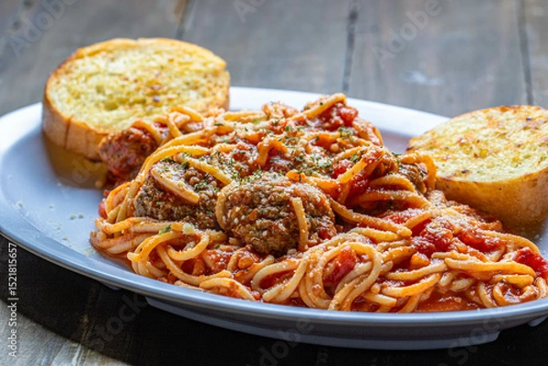 Fototapeta Tasty pasta with meatball and tomato sauce with slices of garlic toasts served in a white plate.