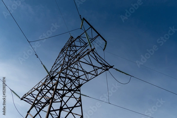 Fototapeta A power transmission tower stands tall against a clear blue sky, with overhead power lines extending in multiple directions on a sunny day