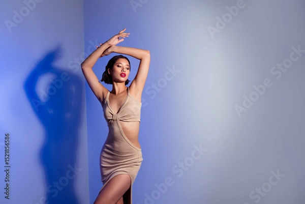 Obraz Confident female model posing gracefully in a stylish beige dress against a blue and white gradient studio background