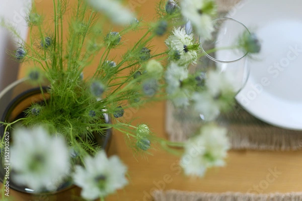 Fototapeta a bouquet of daisies in a glass vase stands on a table on a white background, a wine glass, table setting, plates, defocus, macrophotography, bokeh