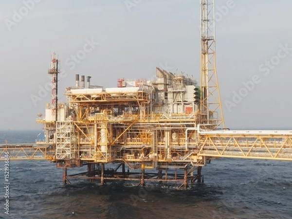 Obraz Imposing offshore oil platform, a testament to human engineering, stands resilient against the vast oceans relentless waves under a calm, hazy sky. A marvel of industrial design.