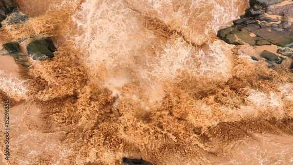 Obraz Bird’s eye perspective captures sediment-rich floodwaters rushing over a barrier, highlighting how extreme weather and global warming amplify natural flood risks. Thailand.
