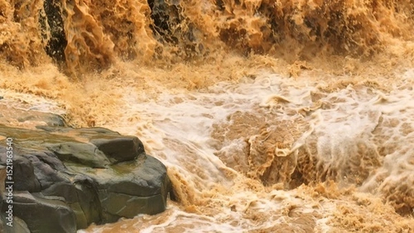 Fototapeta Drone aerial view shows muddy floodwaters cascading forcefully, illustrating the intensified flood events linked to climate change and global warming affecting ecosystems and communities. Thailand.
