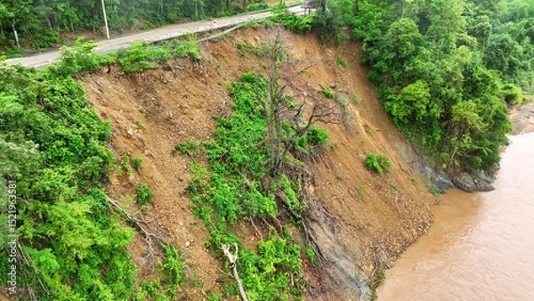 Obraz Aerial drone view of a slope failure adjacent to a river, demonstrating the combined effects of heavy rainfall and deforestation in triggering landslides and environmental degradation.
