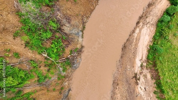 Obraz Overhead shot reveals a muddy riverbank eroded by a recent landslide, emphasizing the role of deforestation and heavy rain in destabilizing slopes and increasing flood risks.
