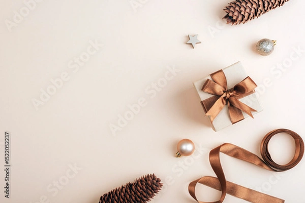 Fototapeta Flat lay with gift box, pine cones and christmas ornaments on soft beige background. Top view, copy space