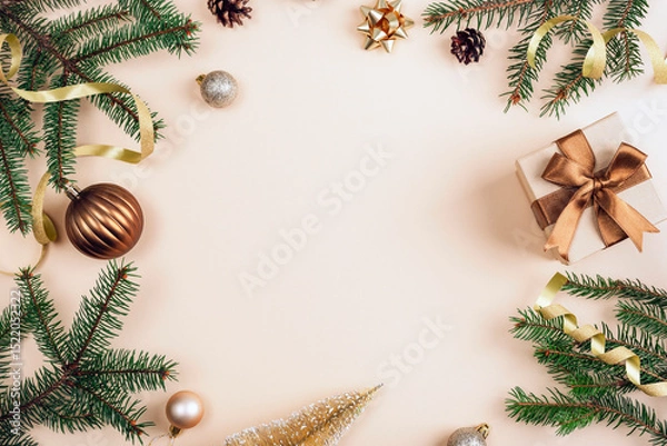Fototapeta Christmas composition with green pine branches, bronze gift boxes with ribbons and ornaments arranged on a beige background. Top view, flat lay, copy space
