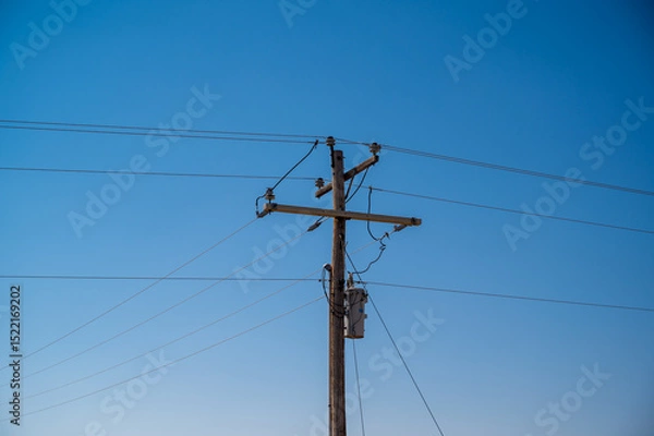 Fototapeta Utility pole stands tall against a clear blue sky in a rural landscape during the afternoon light of late summer