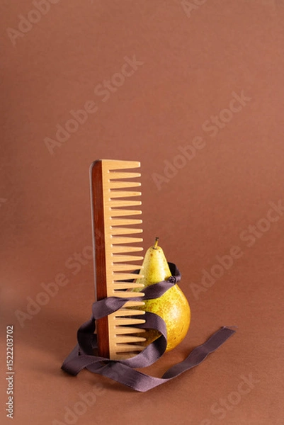 Fototapeta Wooden comb with wide teeth and pear at brown background, contemporary still life composition for modern editorial magazine , Conceptual photo