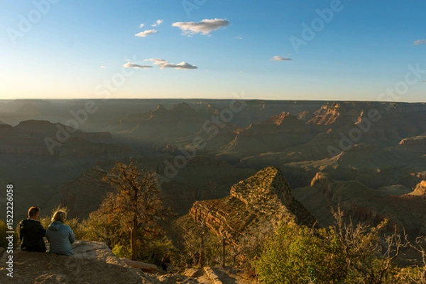 Obraz A breathtaking Grand Canyon sunset reveals layers of rugged red rock formations bathed in warm light and long shadows, while deep canyons and ridges form a mesmerizing view under a clear sky.